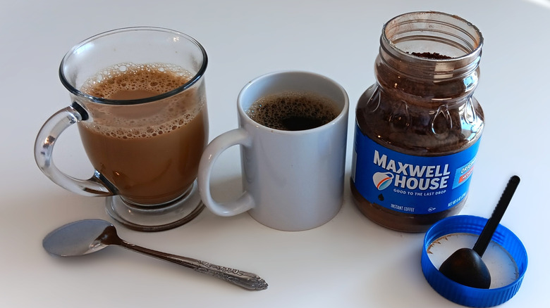 Maxwell House instant coffee in jar with two mugs of coffee, one with cream