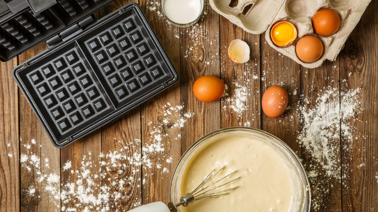 waffle iron, batter in bowl and ingredients milk, eggs and flour