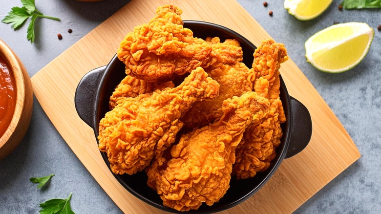 fried chicken drumsticks in a black bowl on a wooden board