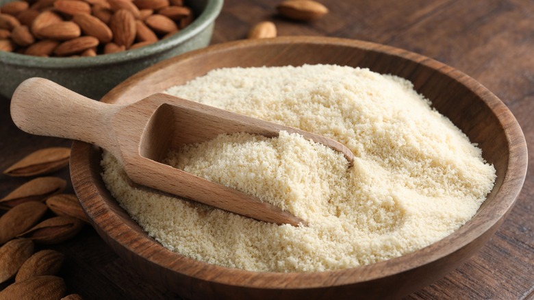 fresh almond flour, scoop in bowl and nuts on wooden table, closeup