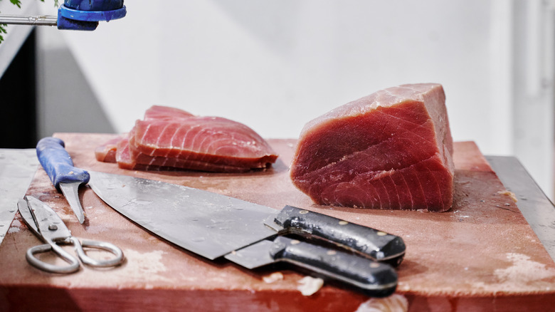 tuna steaks of different sizes stacked on cutting board with knives and scissors