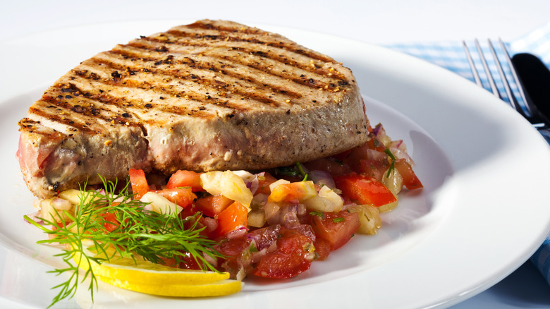 medium-well tuna steak on white plate and bed of diced vegetables with lemon and herb garnish