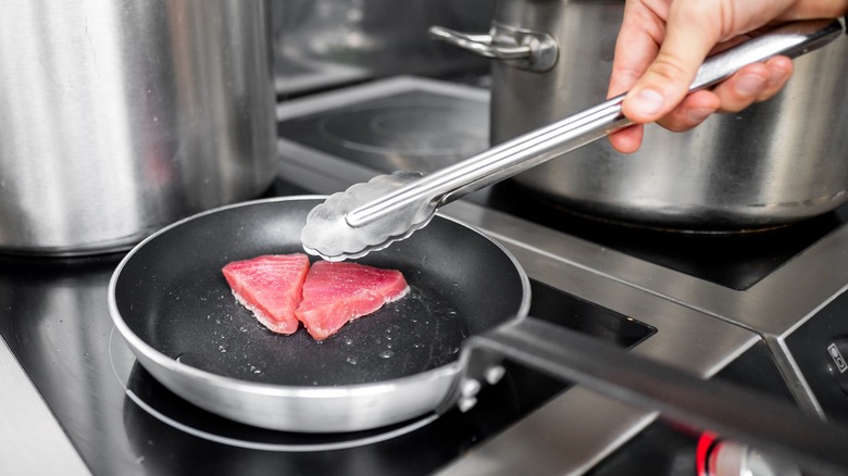 small tuna steaks in pan with excessive moisture and hand with tongs