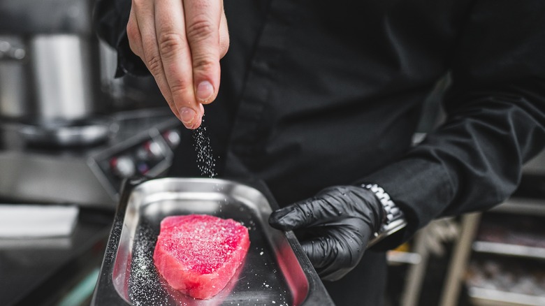 close-up of chef sprinkling seasoning on raw tuna steak in metal dish