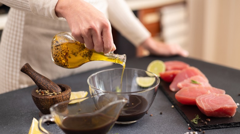 woman adds oil to homemade marinade with raw tuna steaks and mortar and pestle set aside