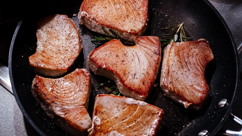 close-up of tuna steaks cooking in pan with rosemary