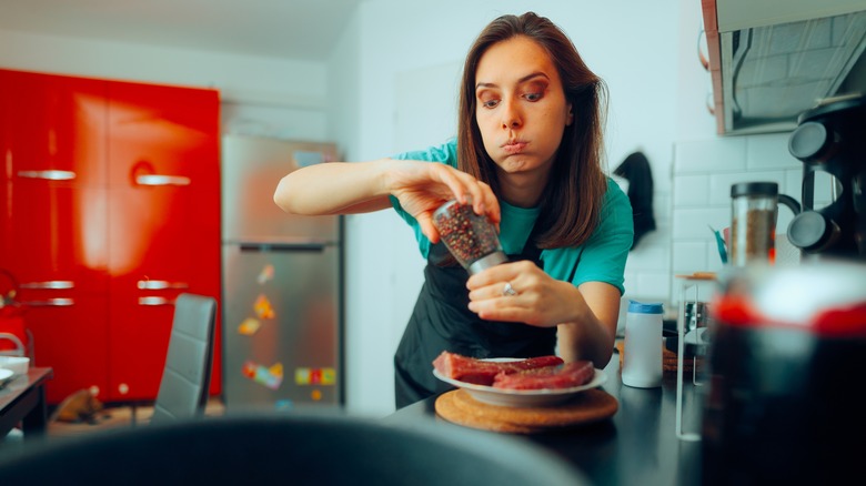 woman with nervous expression seasons raw tuna filets on kitchen counter