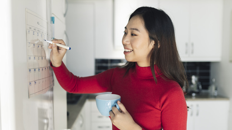 Woman writing with dry erase marker on kitchen calendar