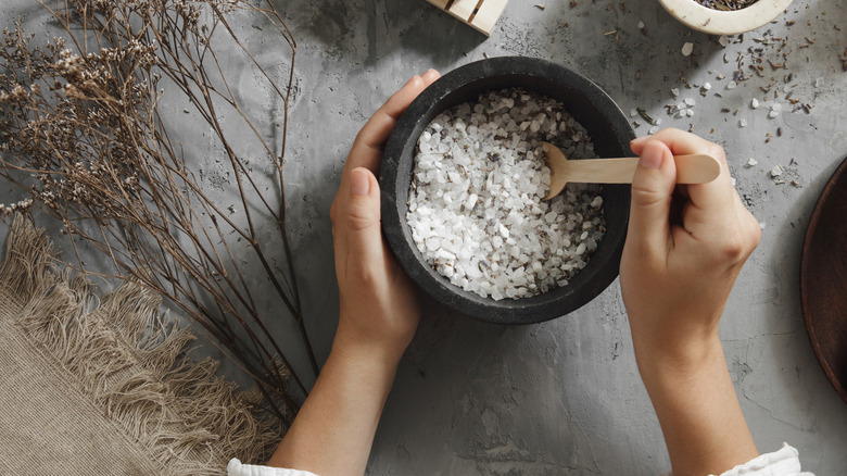 Hands mixing lavender with salt using bowl and spoon