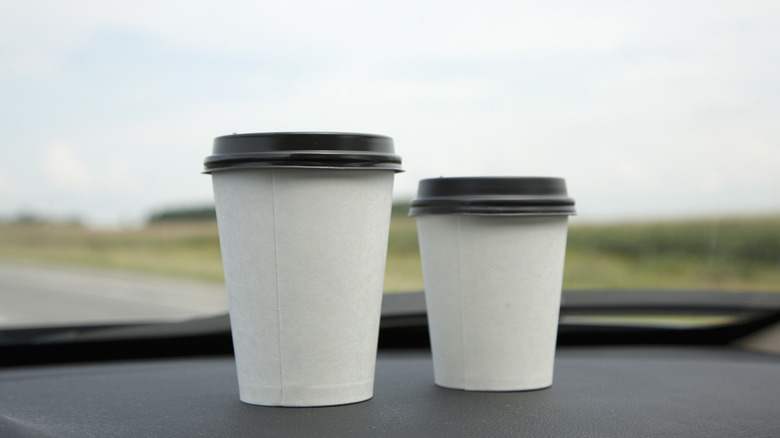 two to-go cups of coffee on a dark counter with nature in the back