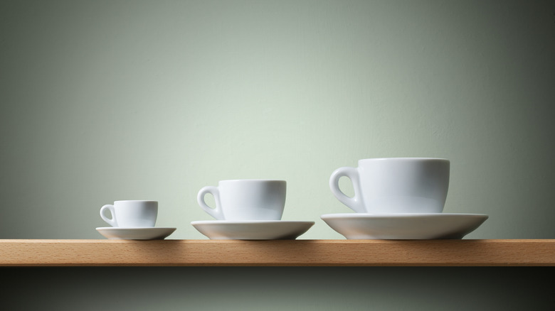 Three white coffee cups of different sizes with plates lined on a wooden counter