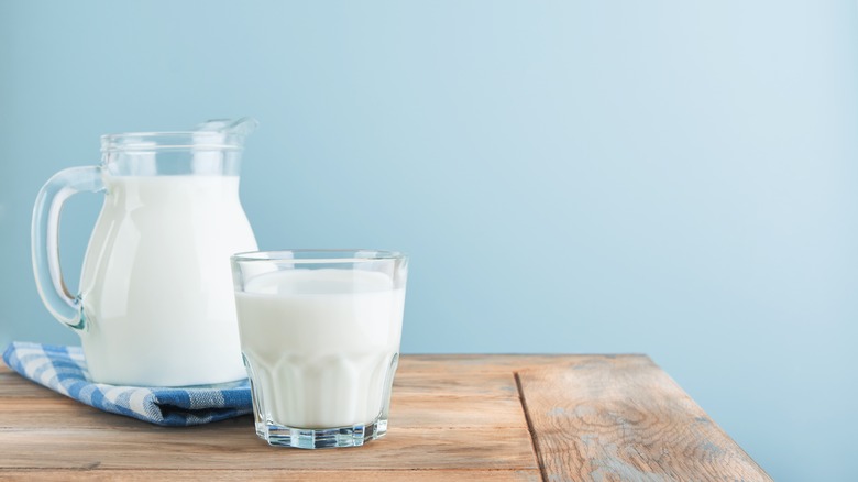 Jug and a glass filled with milk standing on a wooden counter with a light blue background