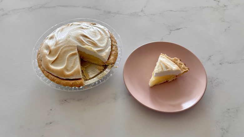 A lemon meringue pie sitting next to a slice of pie on a plate.