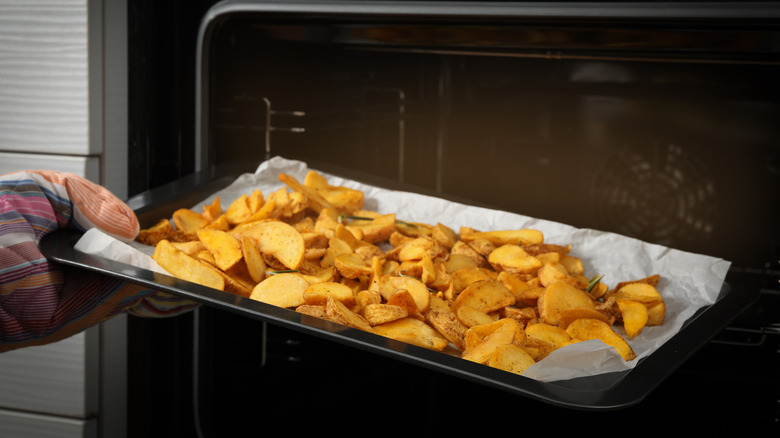 Hand placing baking sheet of fries in oven 