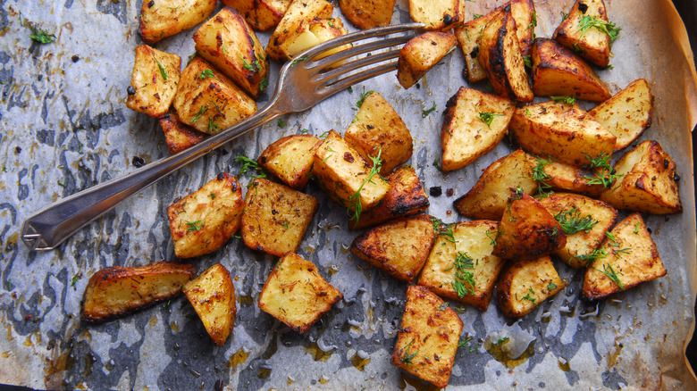 Tray of roast potatoes with herbs and fork