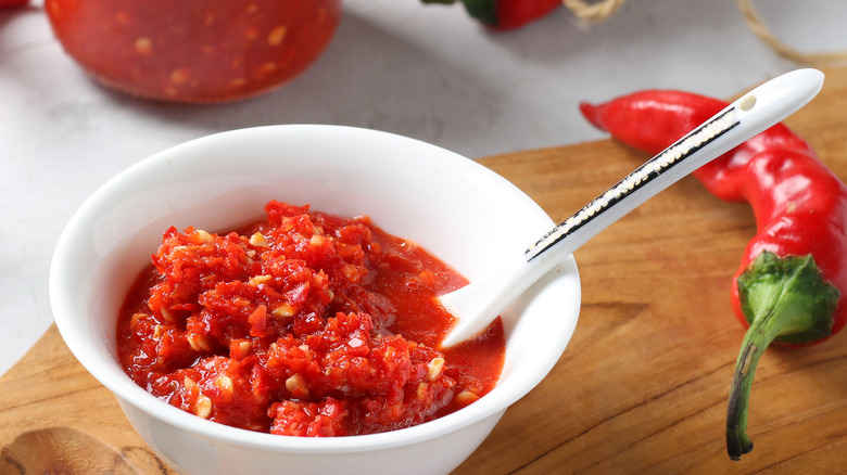 A bowl of harissa on a chopping board with chili peppers