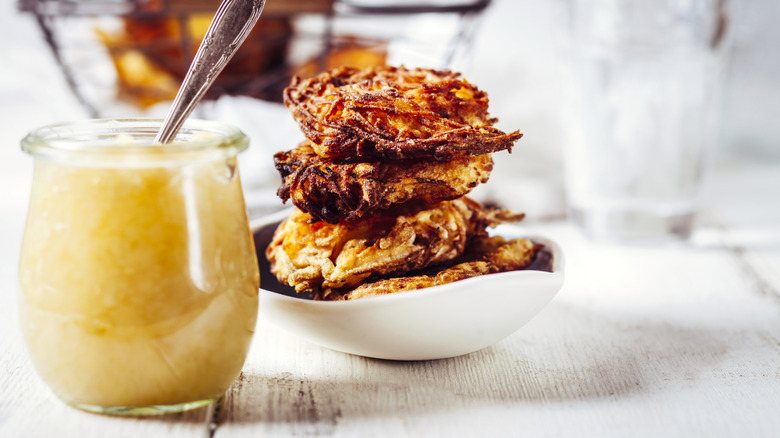 Jar of applesauce next to stacked latkes, bowl