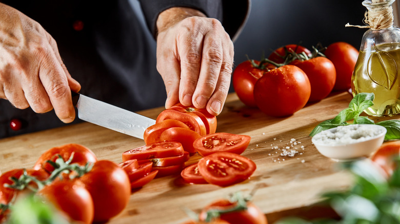 Hands slicing up a tomato