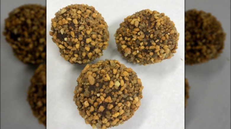 Three chocolate Munchkins covered in nuts on white background