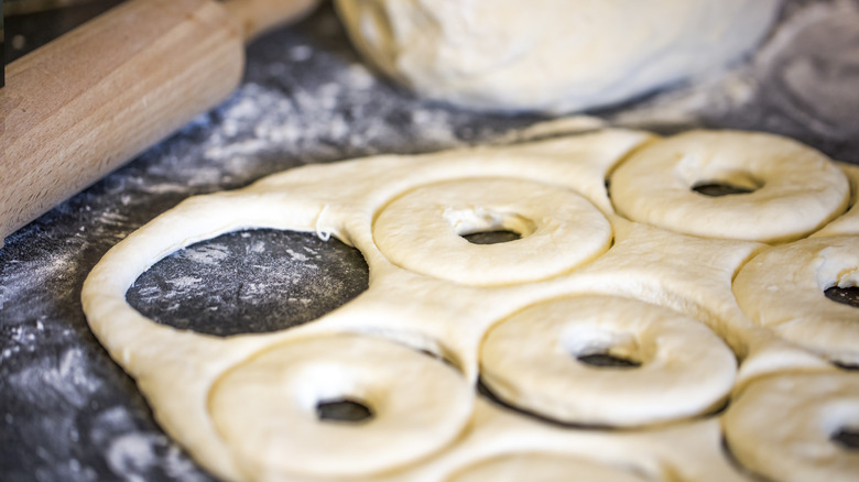 Slab of dough with donut shapes cut out on flour-dusted table