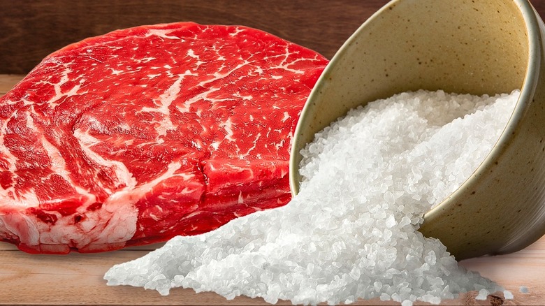 A raw steak next to pouring salt