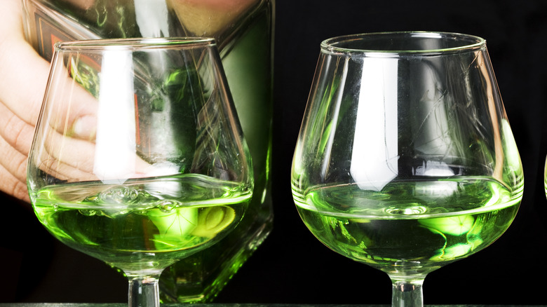 Hand pouring absinthe into two glasses