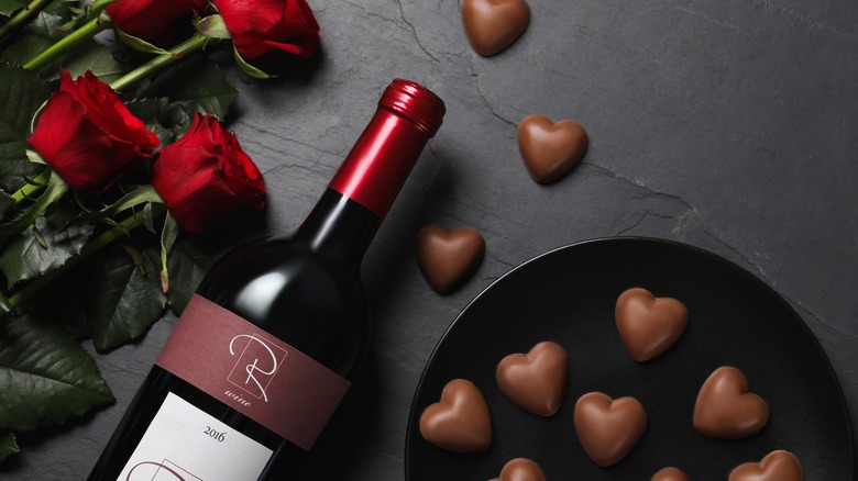 Top-down view of a bottle of red wine, roses, and heart-shaped chocolates