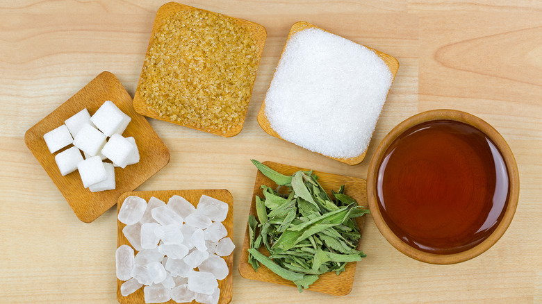 honey, sugar cubes, dark sugar, and stevia leaves on a wood surface