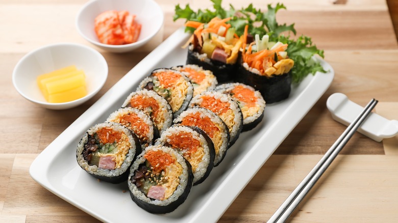 Plated sliced gimbap with chopsticks and banchan