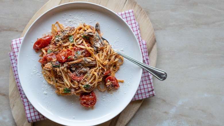 pasta with cherry tomatoes, parmesan, and sardines on a white plate over a wood board