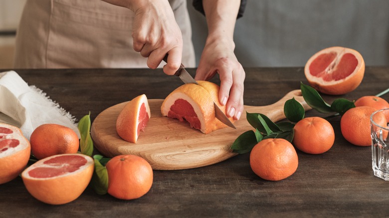 A person cutting grapefruit on a cutting board
