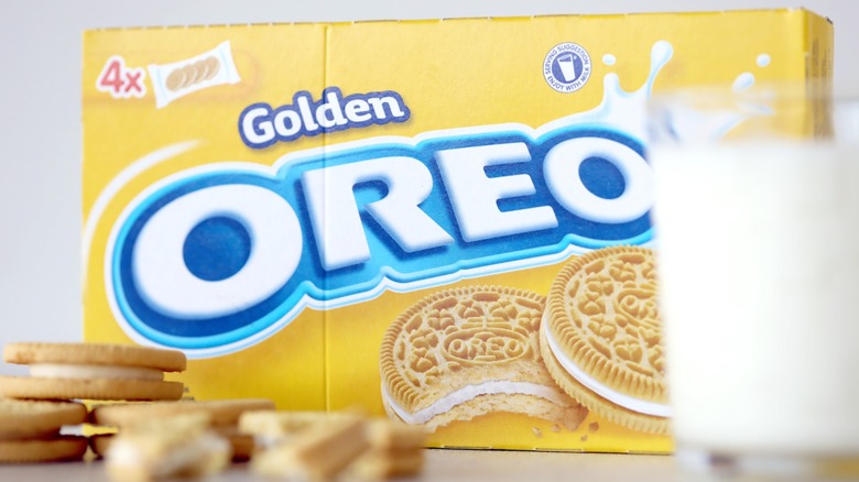 A package of Golden Oreos in the background, with the cookies and a glass of milk in the foreground