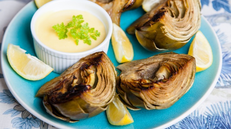 Grilled artichokes, lemon wedges, and aioli on a blue plate