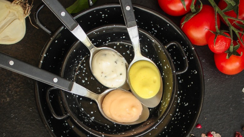 pans holding spoons of sauce, remoulade, tartar, and rouille, tomatoes in background 