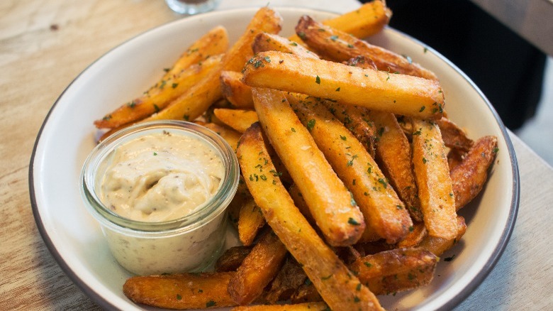 A bowl of fries with a side of aioli on a wooden table