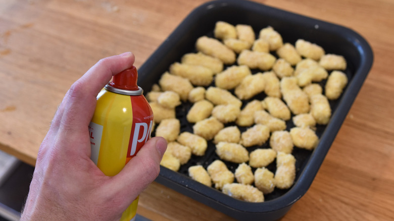 hand spraying cheese curds with cooking spray