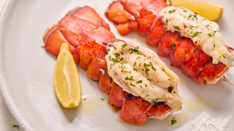 Butterflied lobster tails on a plate with lemon wedges
