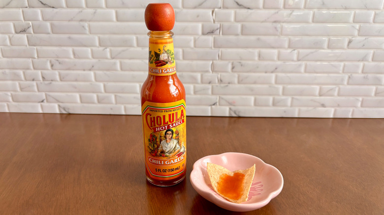 Cholula chili garlic hot sauce bottle next to tortilla chip