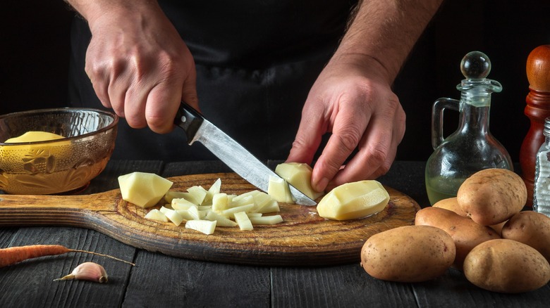 Hands cutting peeled potatoes