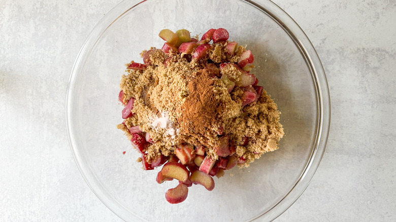 Sliced rhubarb, brown sugar, cinnamon, ginger, and salt in glass mixing bowl