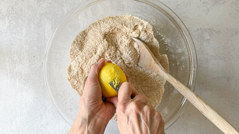 Zesting a lemon over a bowl of dry ingredients in mixing bowl with wooden spoon