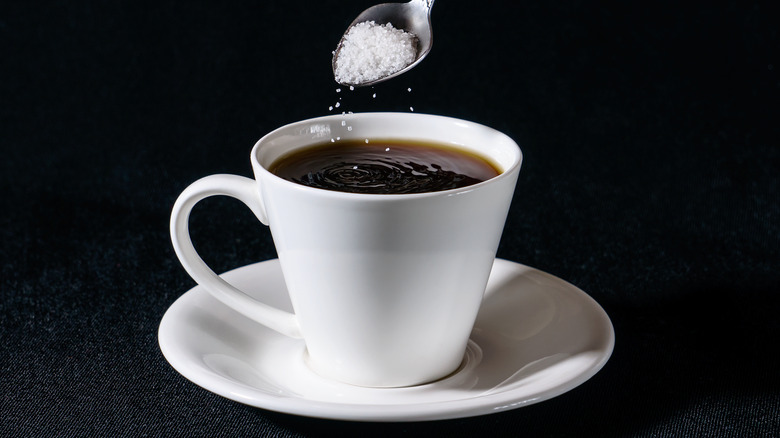 Spoon adding salt to a cup of coffee