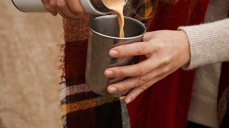 Person's hands pouring coffee with milk out of thermos