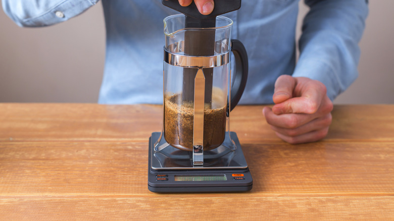 Hand stirring the grounds in a French press on a scale