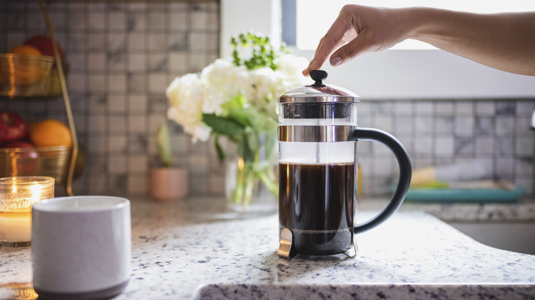 Hand pressing down French press plunger on a kitchen counter