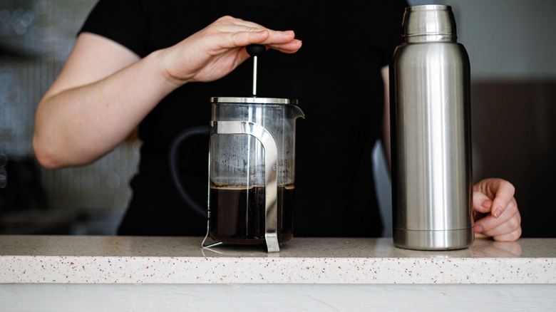 Hand plunging a French press near a Thermos