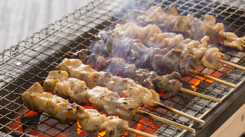 skewers of meat grilling on wire grid 