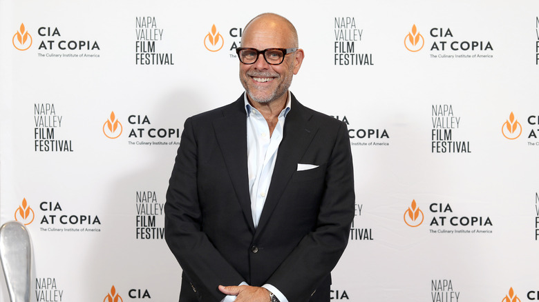 Alton Brown smiling in glasses and suit at event