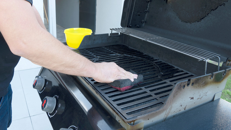 Person cleaning grill with sponge