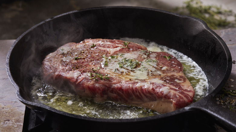 steak cooking in a cast iron pan with garlic and herbs